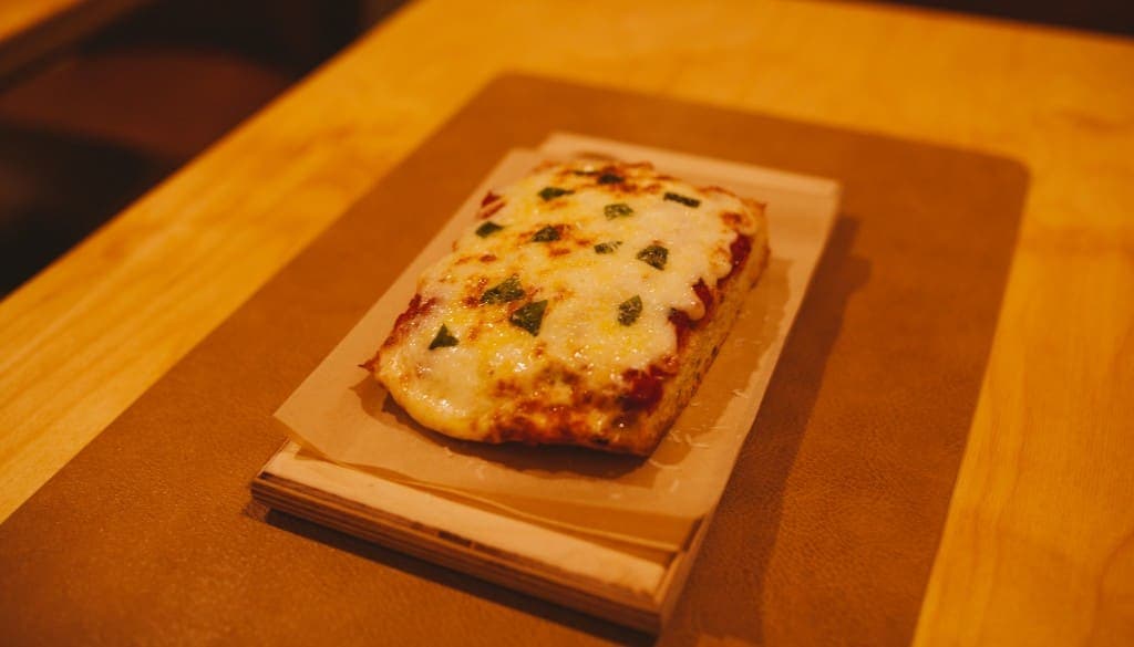 Cheese pizza slice on a wooden board at The Analogue Room in Solvang