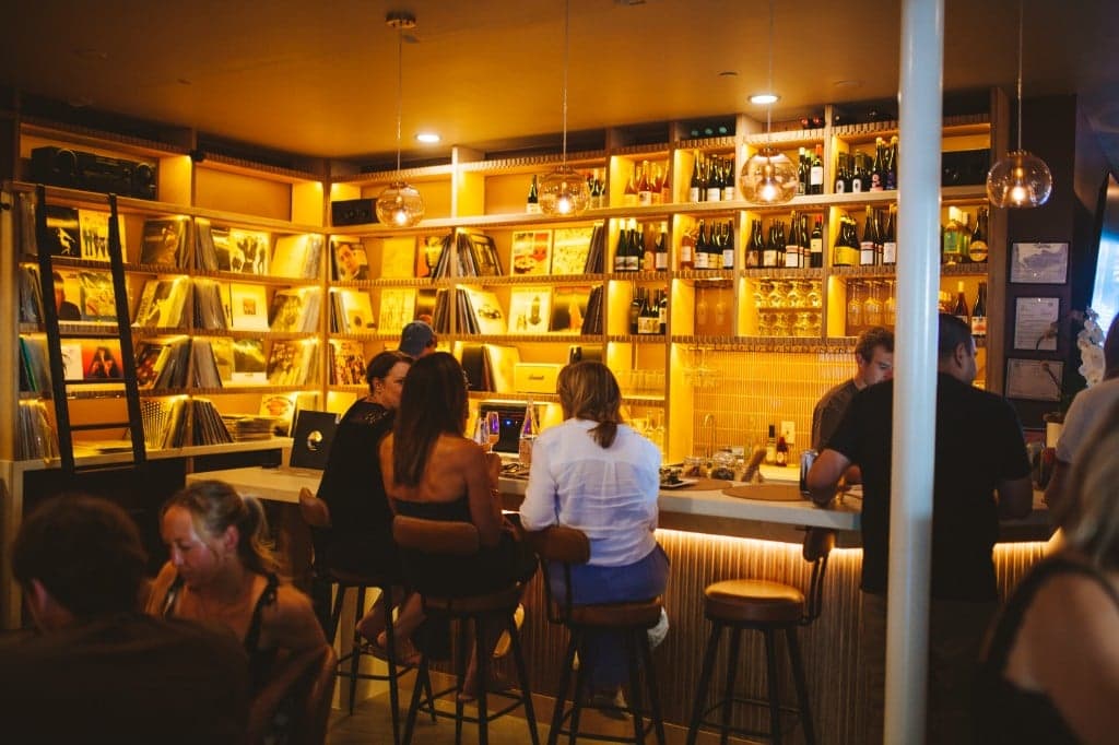 Guests at the bar with vinyl shelves and wine bottles at Analogue Room in Solvang