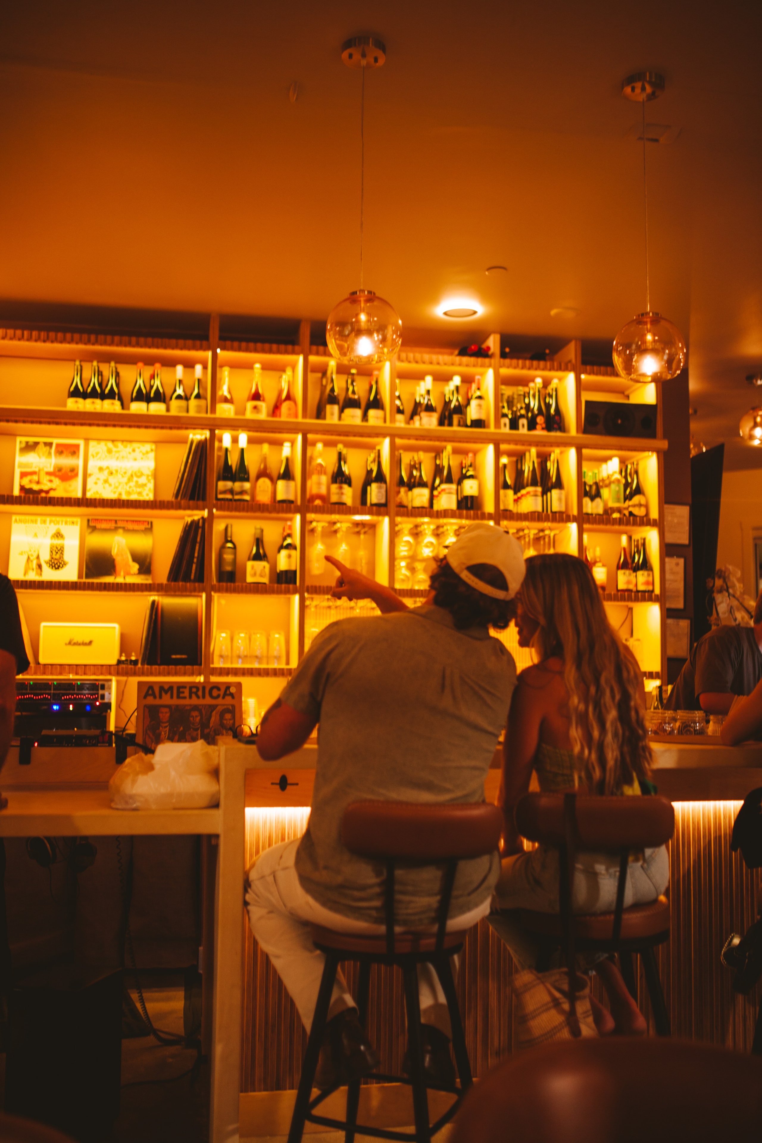 Guests at the bar choosing from the backlit wine and vinyl wall at Analogue Room in Solvang